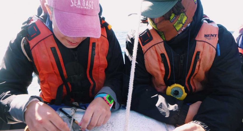 Two people wearing life jackets and hates examine a map. 